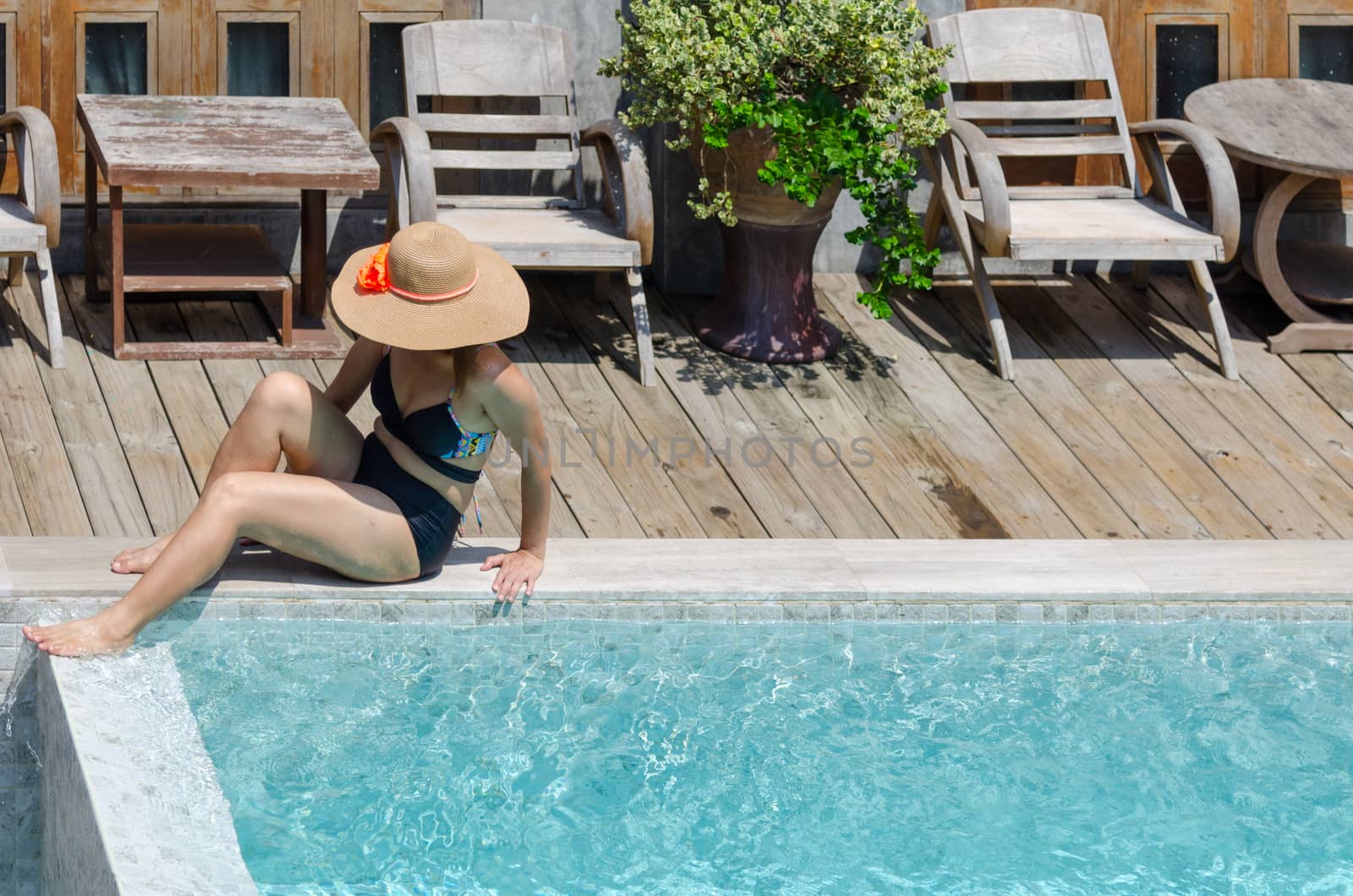 Beautiful young woman sitting by the pool wearing a brown hat.