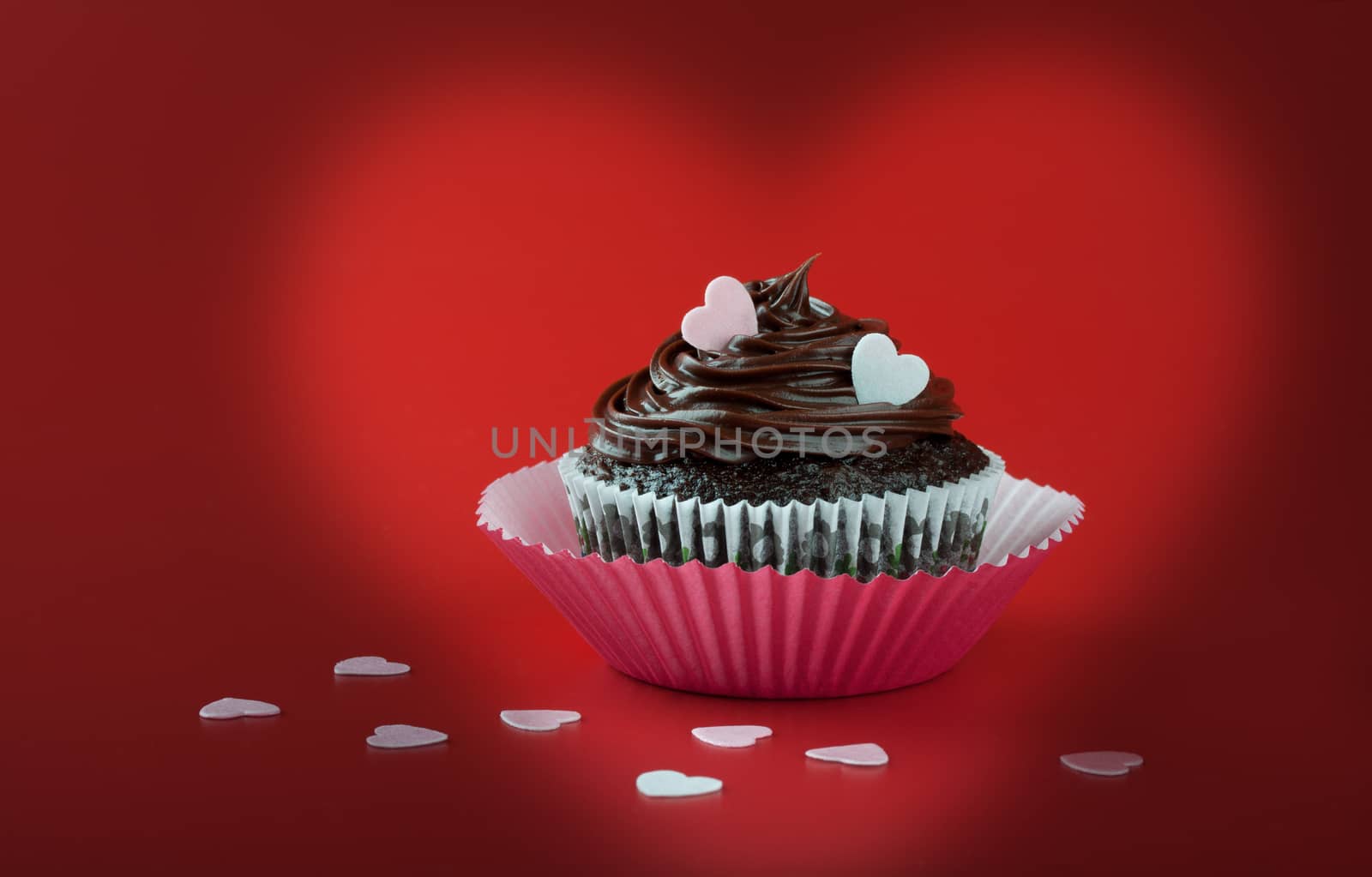 Chocolate cupcake with pink eatable hearts on red background by lanalanglois