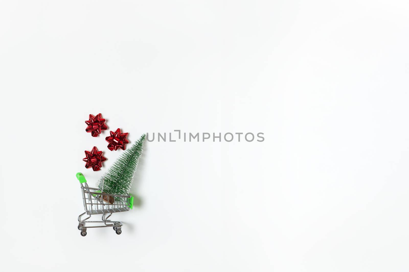 Christmas snow covered fir and red bows for gift in toy shopping cart on white background, copy space. New Year, sales, online shopping concept. Horizontal, flat lay. Minimal style. Top view.