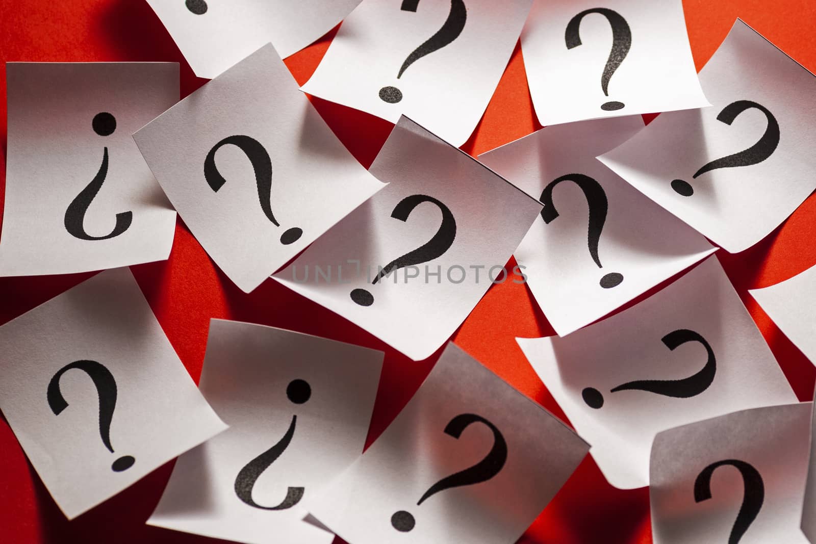 Randomly scattered question marks on white paper over a colorful red background in a conceptual image