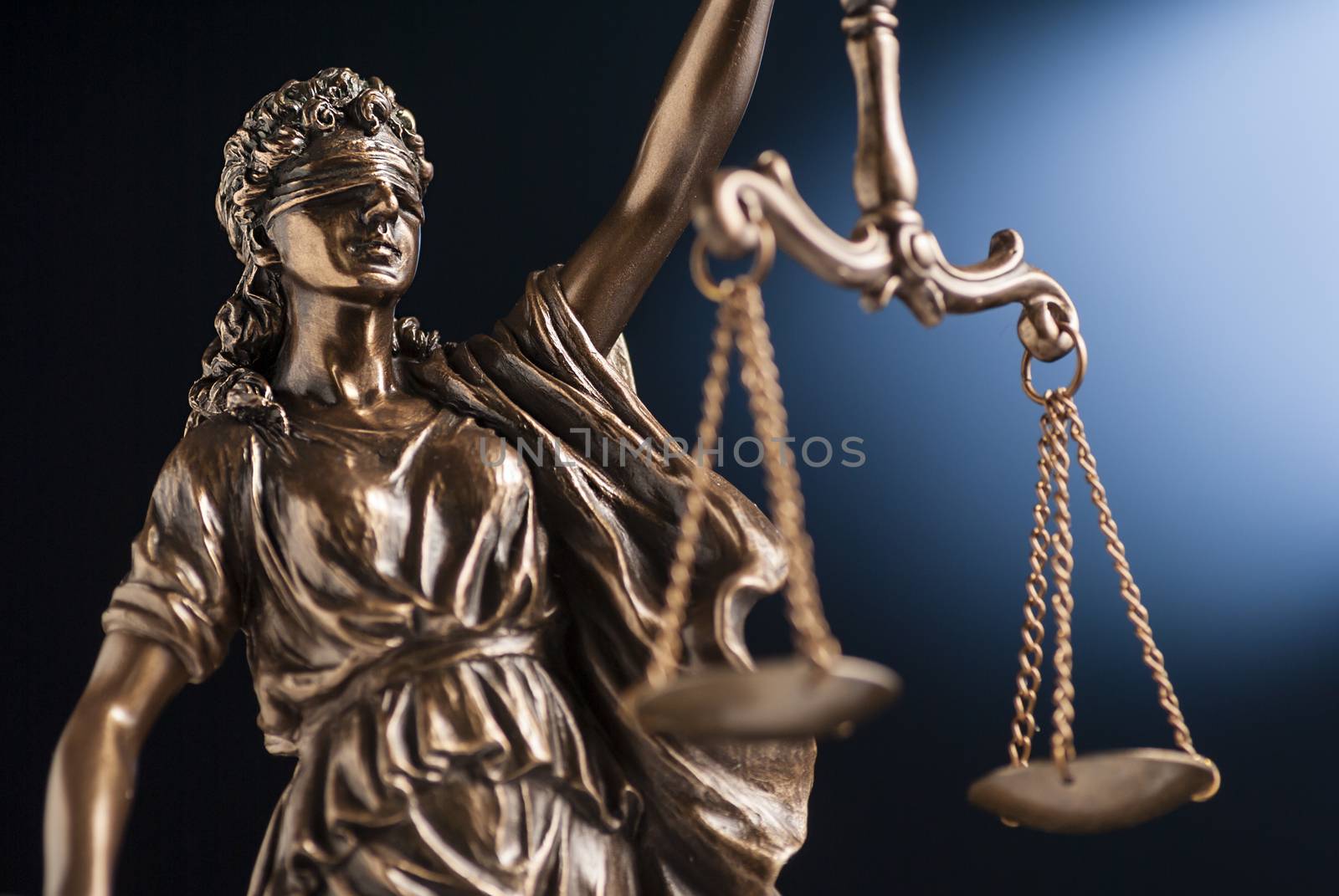 Bronze statue of Lady Justice wearing a blindfold holding up scales representing law and order over a blue background with copy space