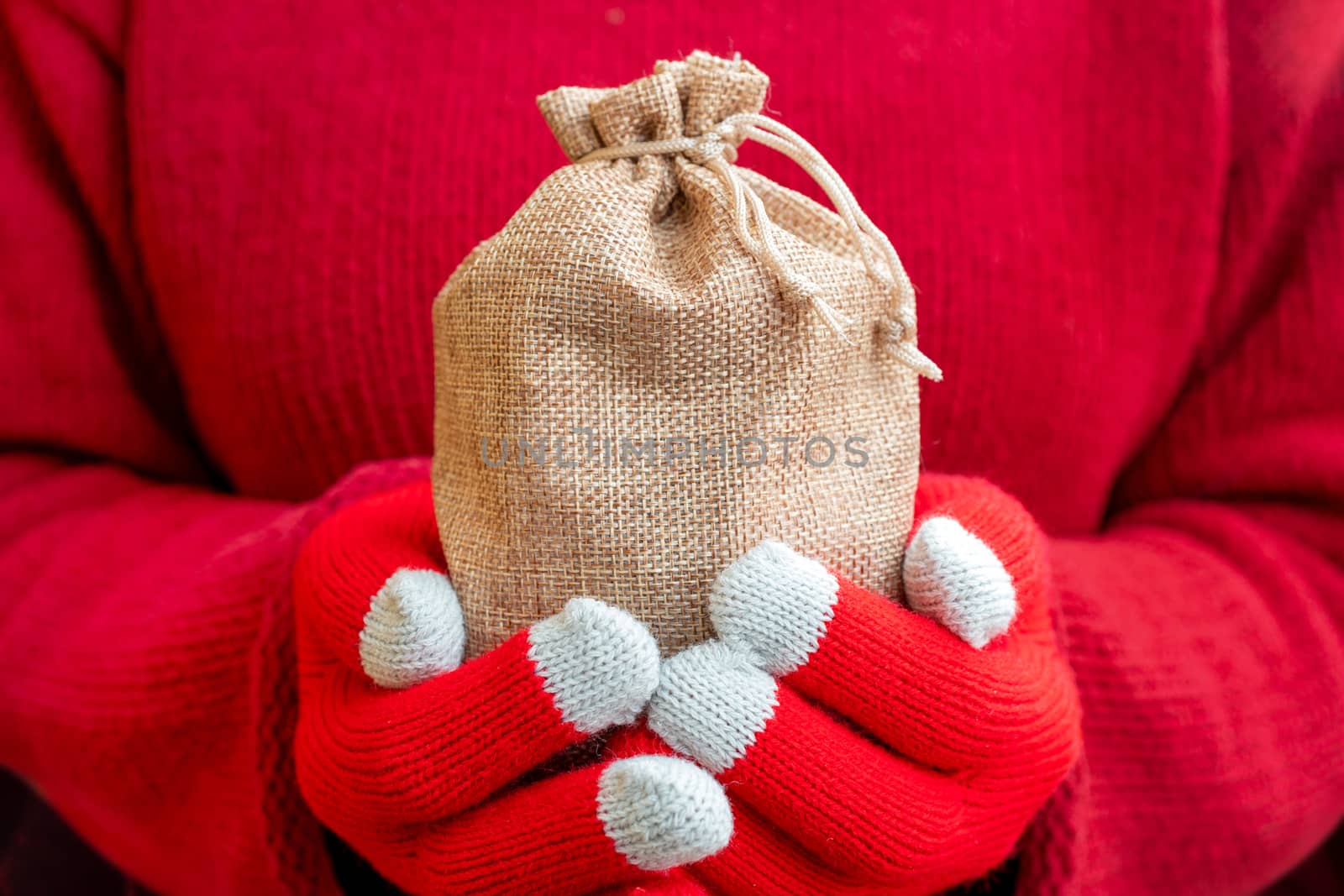 Christmas gifts bag in female hands. Red knitted gloves and a sweater.