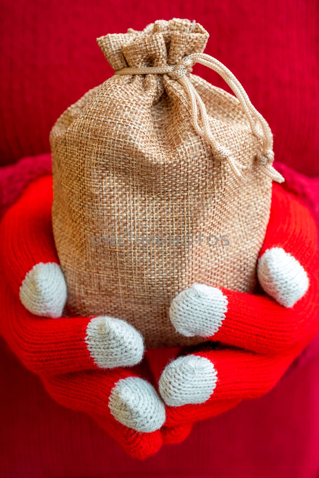 Christmas gifts bag in female hands. Red knitted gloves and a sweater.