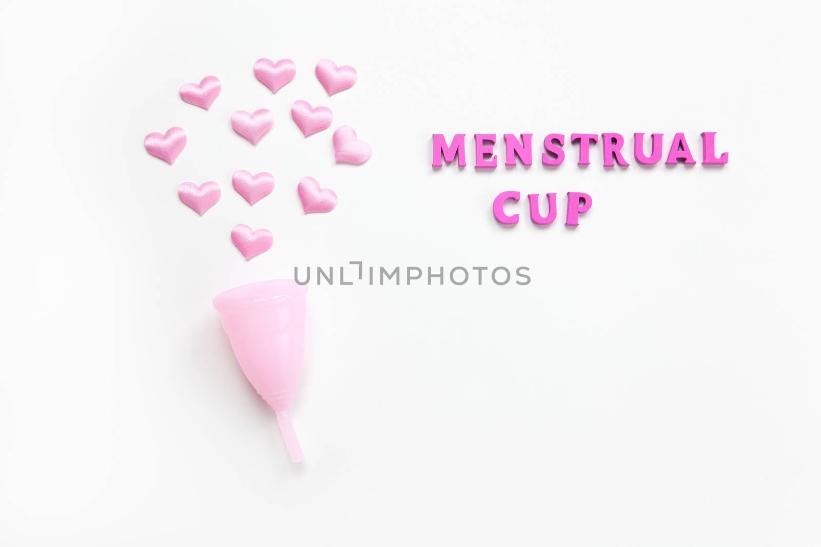 Pink menstrual cup on white background with small hearts and inscription. Concept zero waste, savings, environmental conservation, sustainable lifestyle. Feminine hygiene product, flatlay. Horizontal.