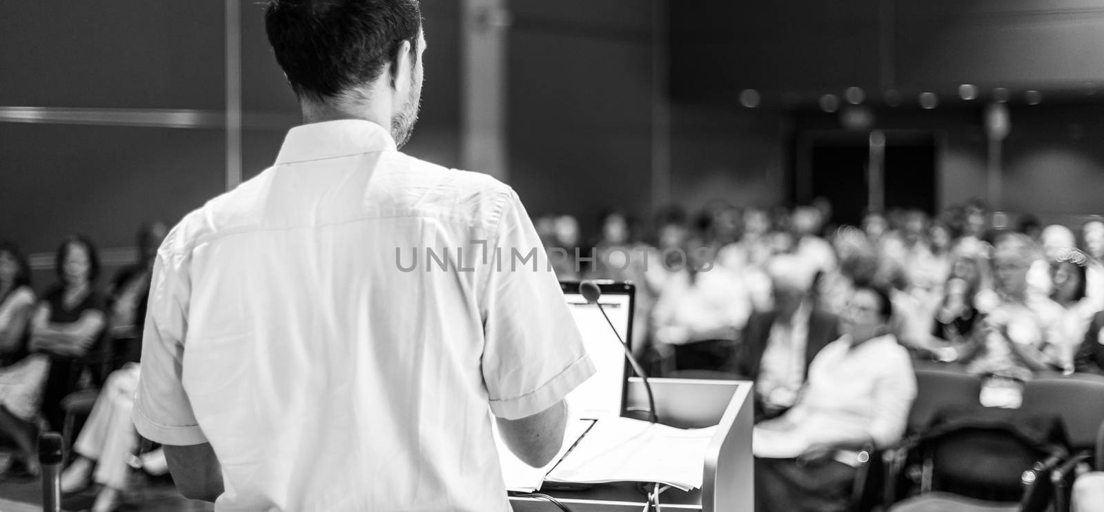 Speaker giving a talk on corporate business conference. Unrecognizable people in audience at conference hall. Business and Entrepreneurship event. Black and white image.