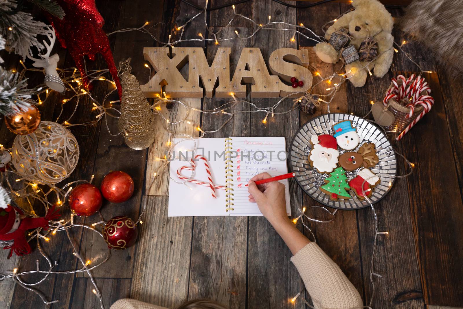 Writing out a Christmas list on rustic timber floor with Christmas decorations, fairy lights  and festive gingerbread.  Christmas scene background