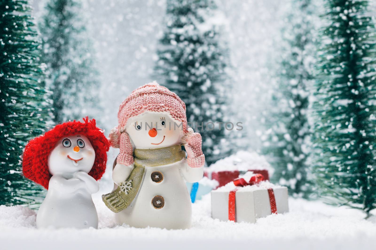 Two small cute snowmen friends with gifts in forest under falling snow