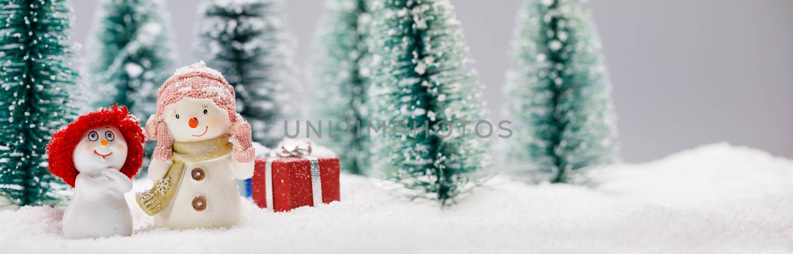 Two small cute snowmen friends with gifts in forest under falling snow