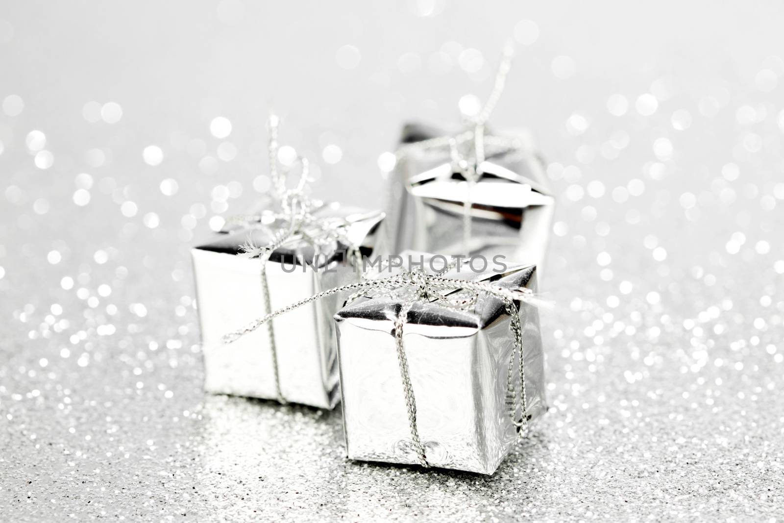 Decorative silver boxes with holiday gifts on shiny glitter background