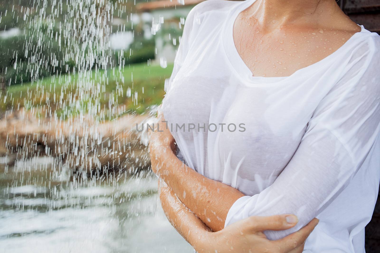 Attractive young female in wet blouse looking away while standing near splashing clean water in resort