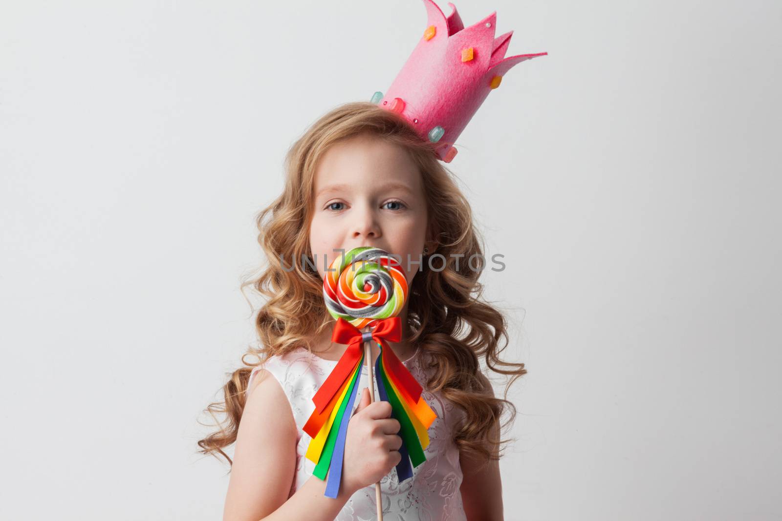 Beautiful little candy princess girl in crown holding big lollipop and smiling