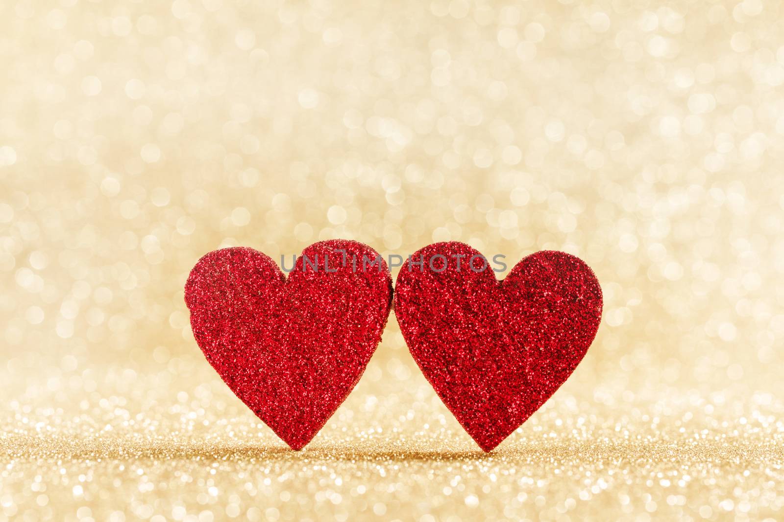 Two small handmade red glitter hearts on bright golden lights bokeh background Valentines day card