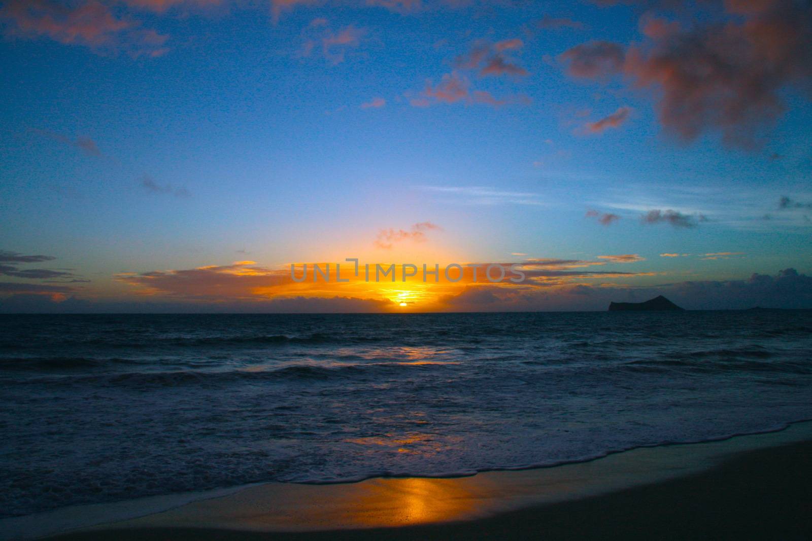 In images Rising sun on the horizon above a calm ocean or sea. On the blue sky white clouds