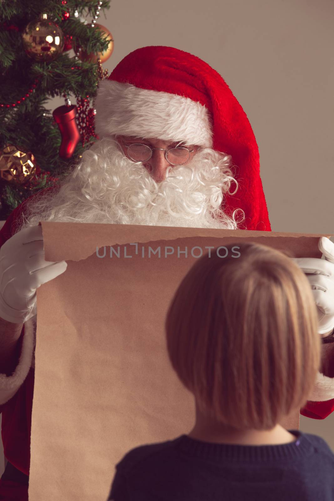 Santa Claus with with list or nice or naugthy list paper with small boy near christmas tree