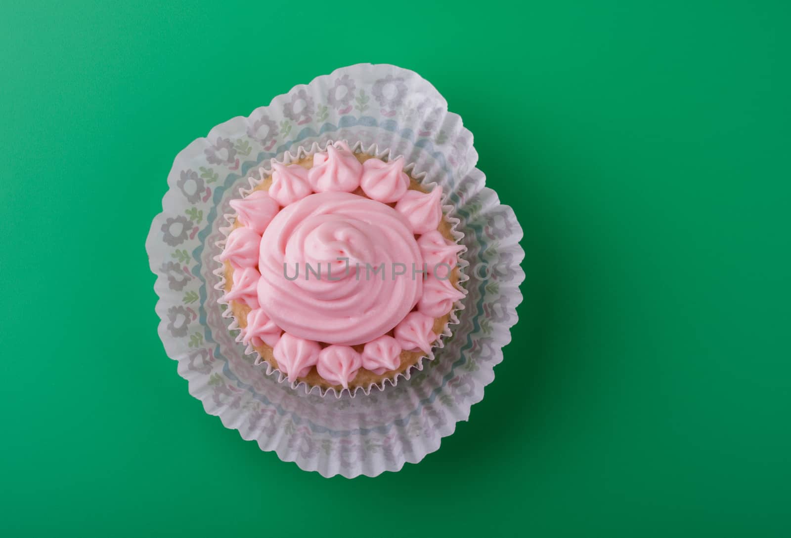 Delicious sweet vanilla cupcake with pink icing sugar, green background