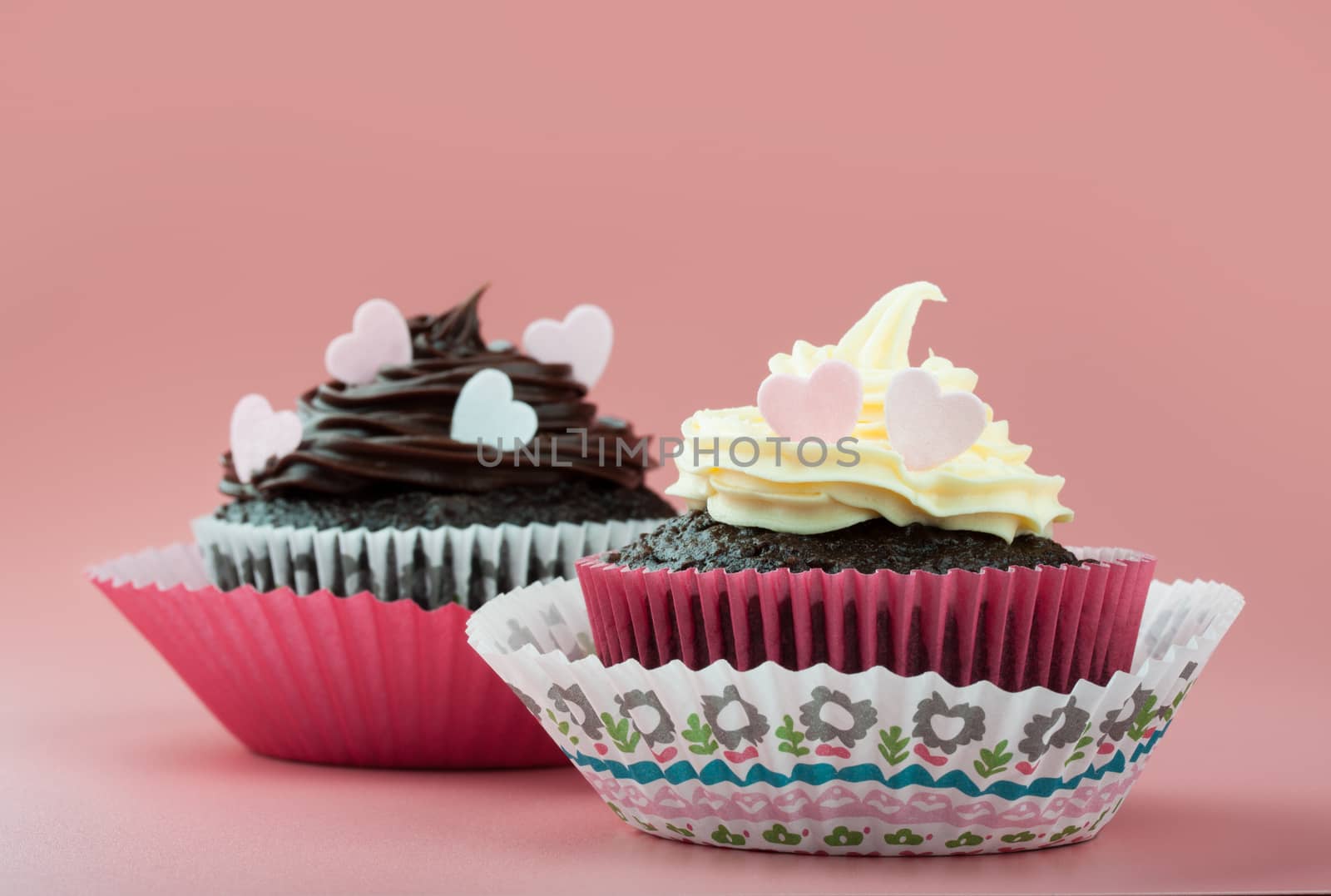 chocolate cupcake with vanilla chocolate icing and eatable hearts, in nice decorative paper mold, pink background