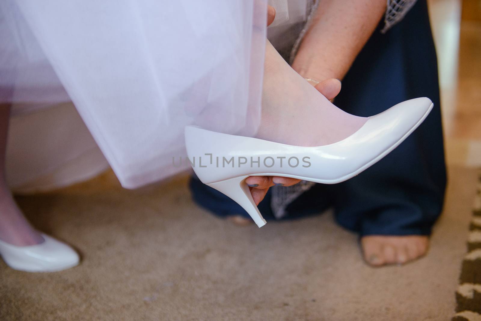 Bridesmaid helping slender bride lacing her wedding white dress, buttoning on delicate lace pattern with fluffy skirt on waist. Morning bridal preparation details newlyweds. Wedding day moments, wear. by Brejeq