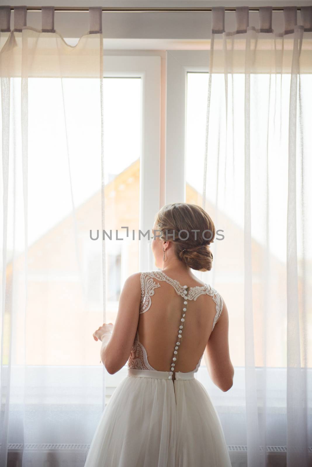 Bridesmaid helping slender bride lacing her wedding white dress, buttoning on delicate lace pattern with fluffy skirt on waist. Morning bridal preparation details newlyweds. Wedding day moments, wear.