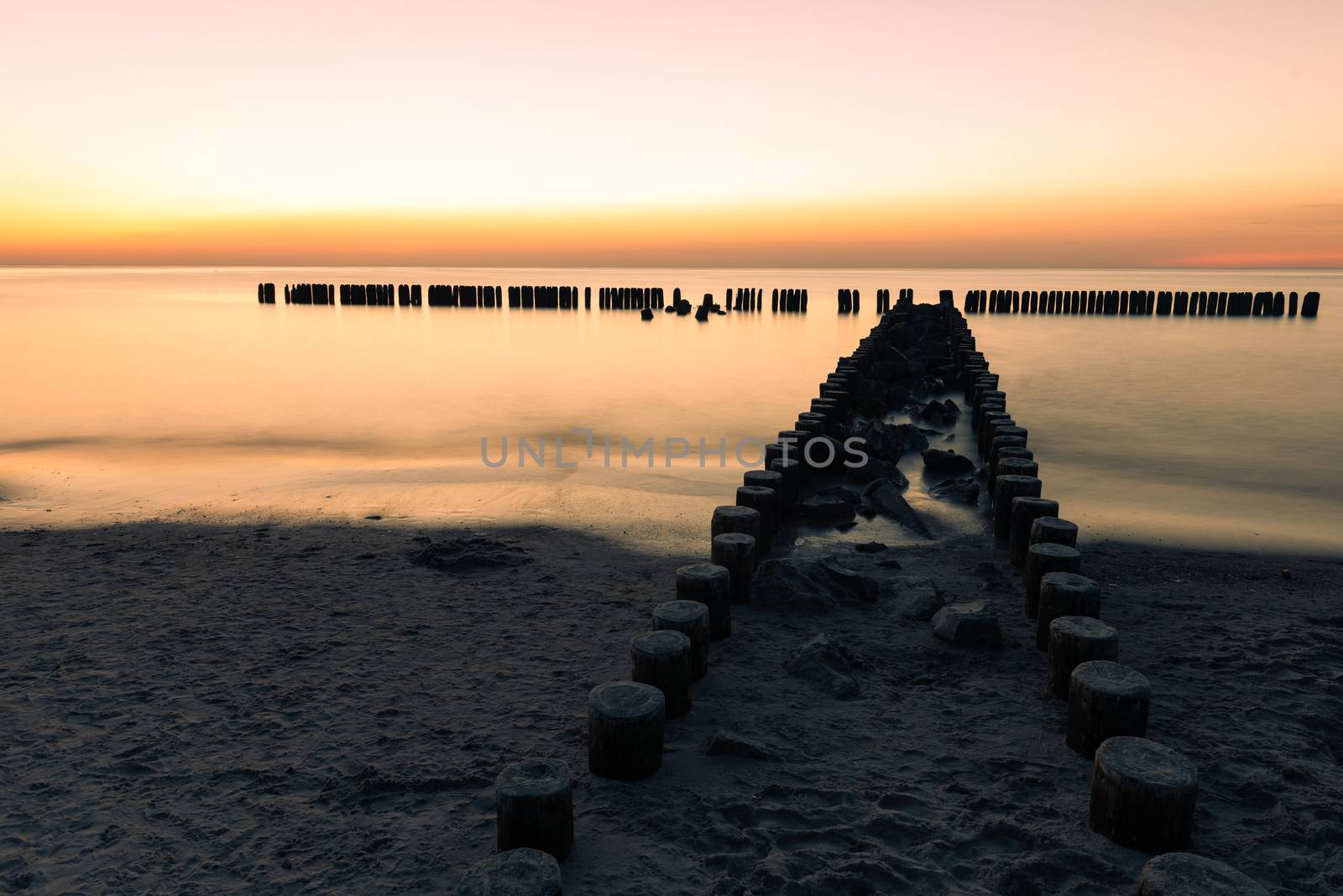 A photograph of wooden breakwater and seagulls at sunset on the Baltic Sea
