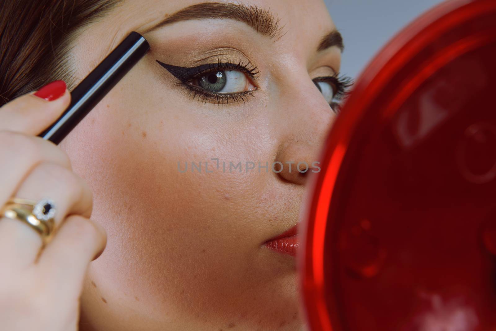 Beauty model teenage girl looking in the mirror and applying mascara make up. Beautiful young woman apply makeup by Brejeq