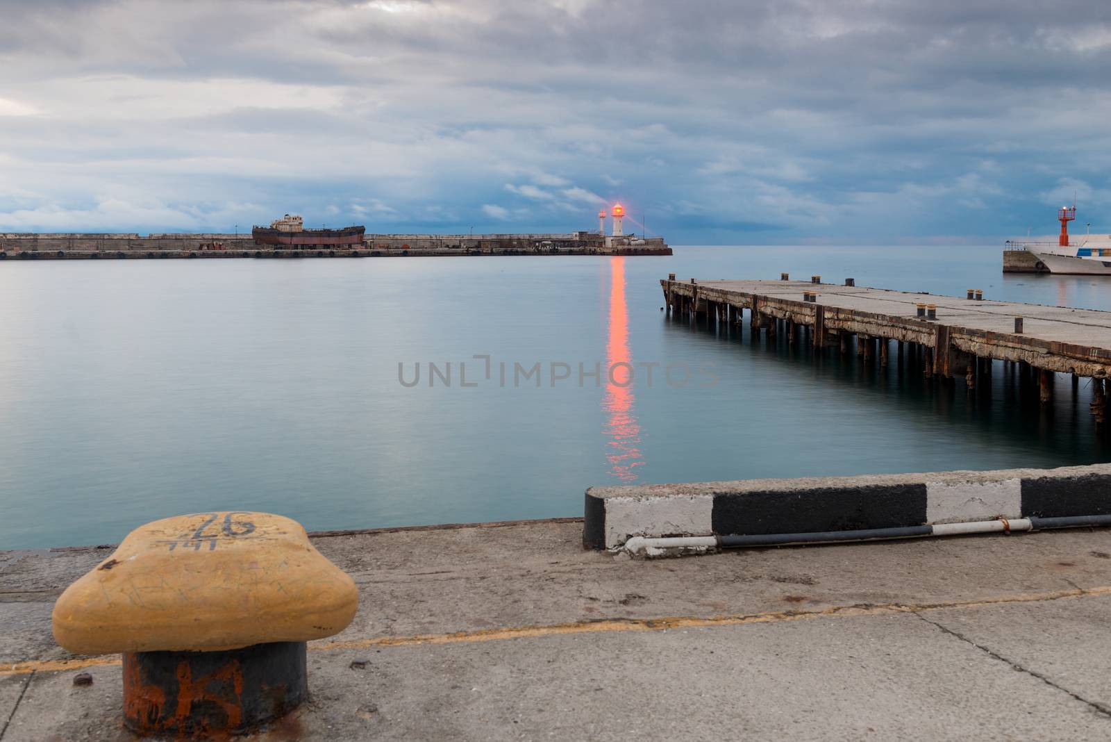 Embankment, pier and lighthouse with bright red light on the seashore at dusk