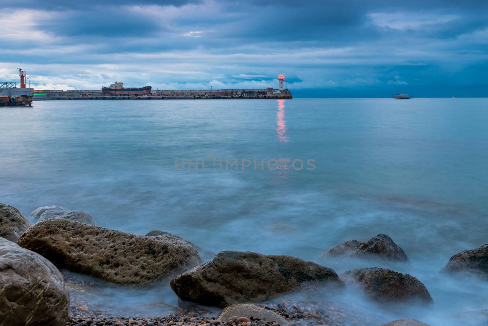 view of the lighthouse on the seashore at dusk, rainy clouds over the sea