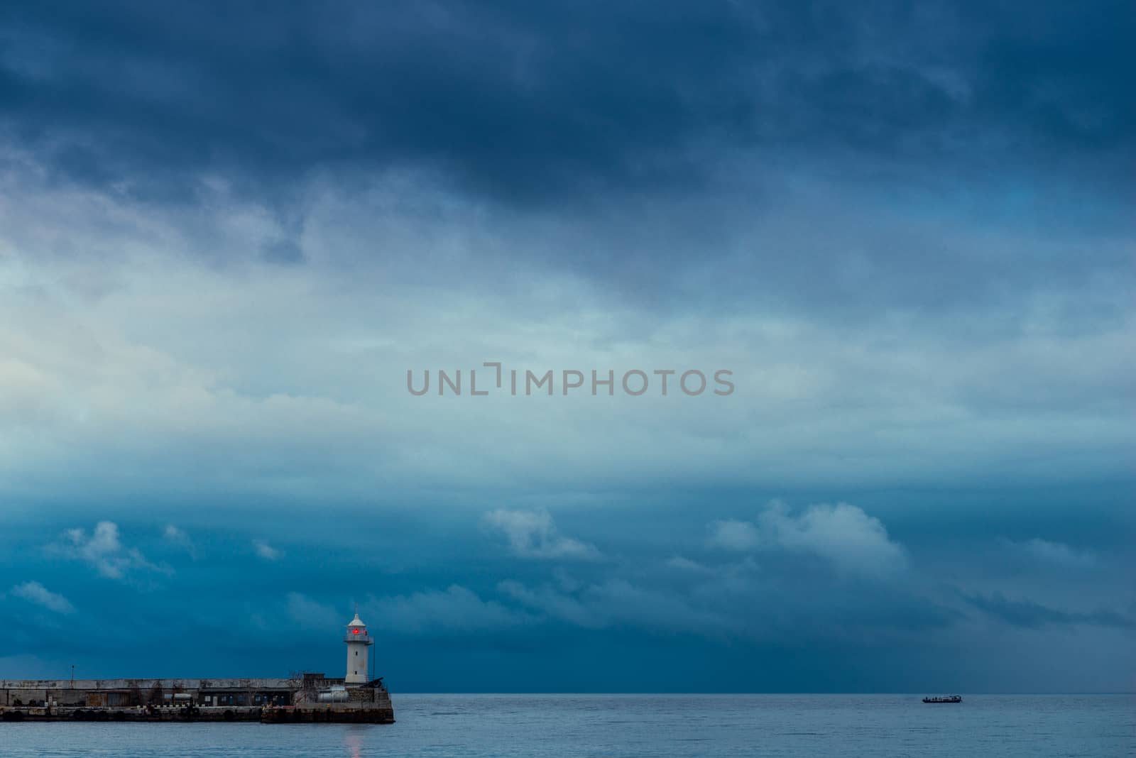 Lonely lighthouse with a red lantern on a background of rainy blue clouds over the sea