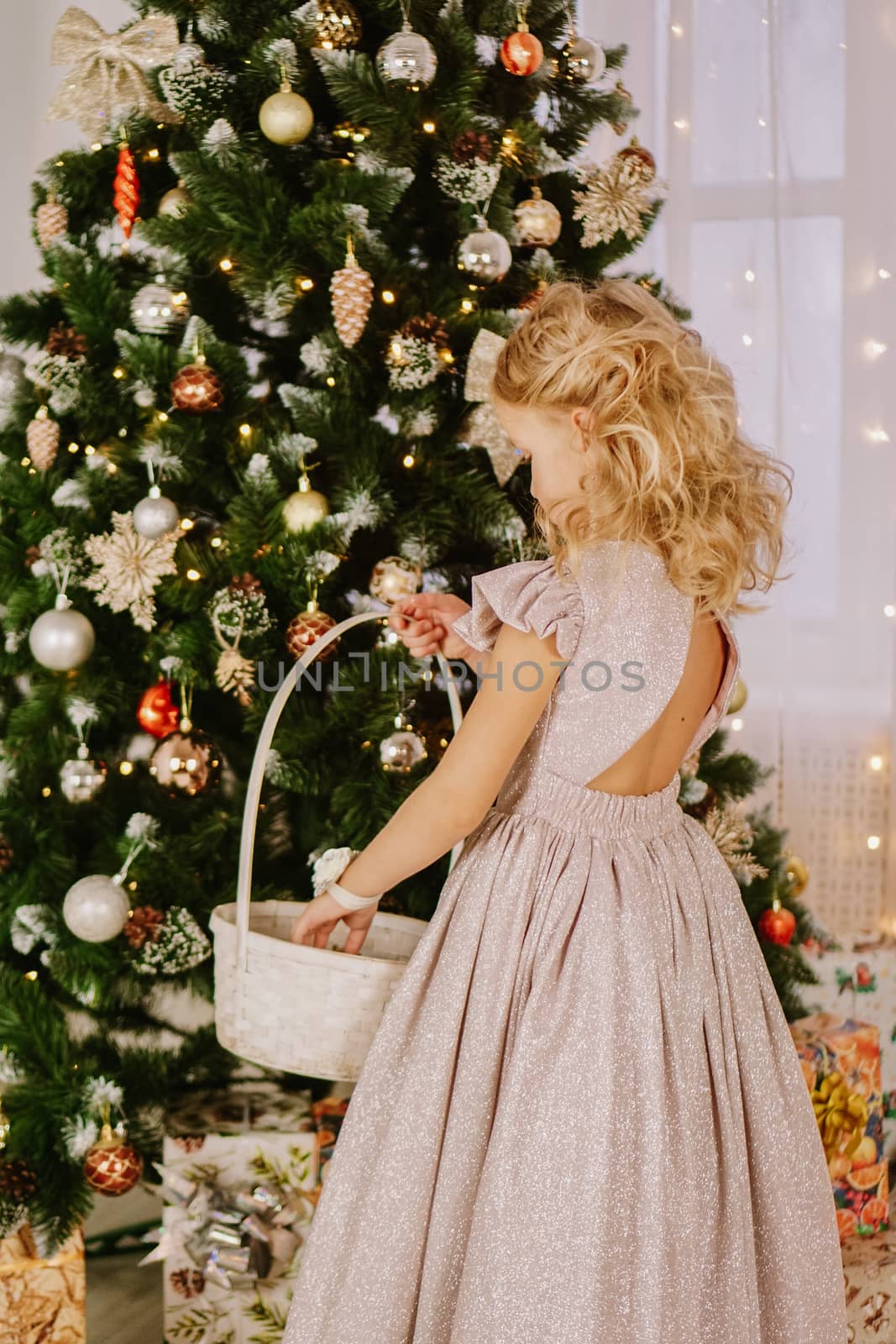 Girl in a pink dress with a wicker basket near the christmas tree