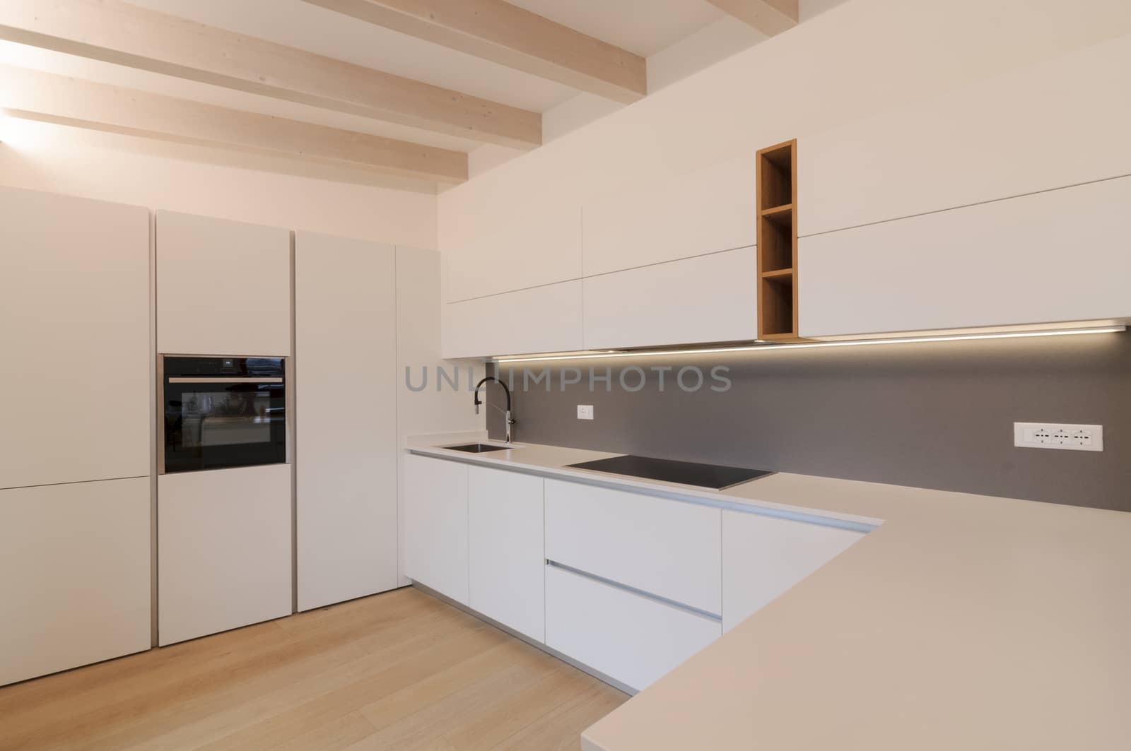 Modern and elegant kitchen interior with white cabinets, induction hob and wooden inserts. Contemporary Scandinavian style