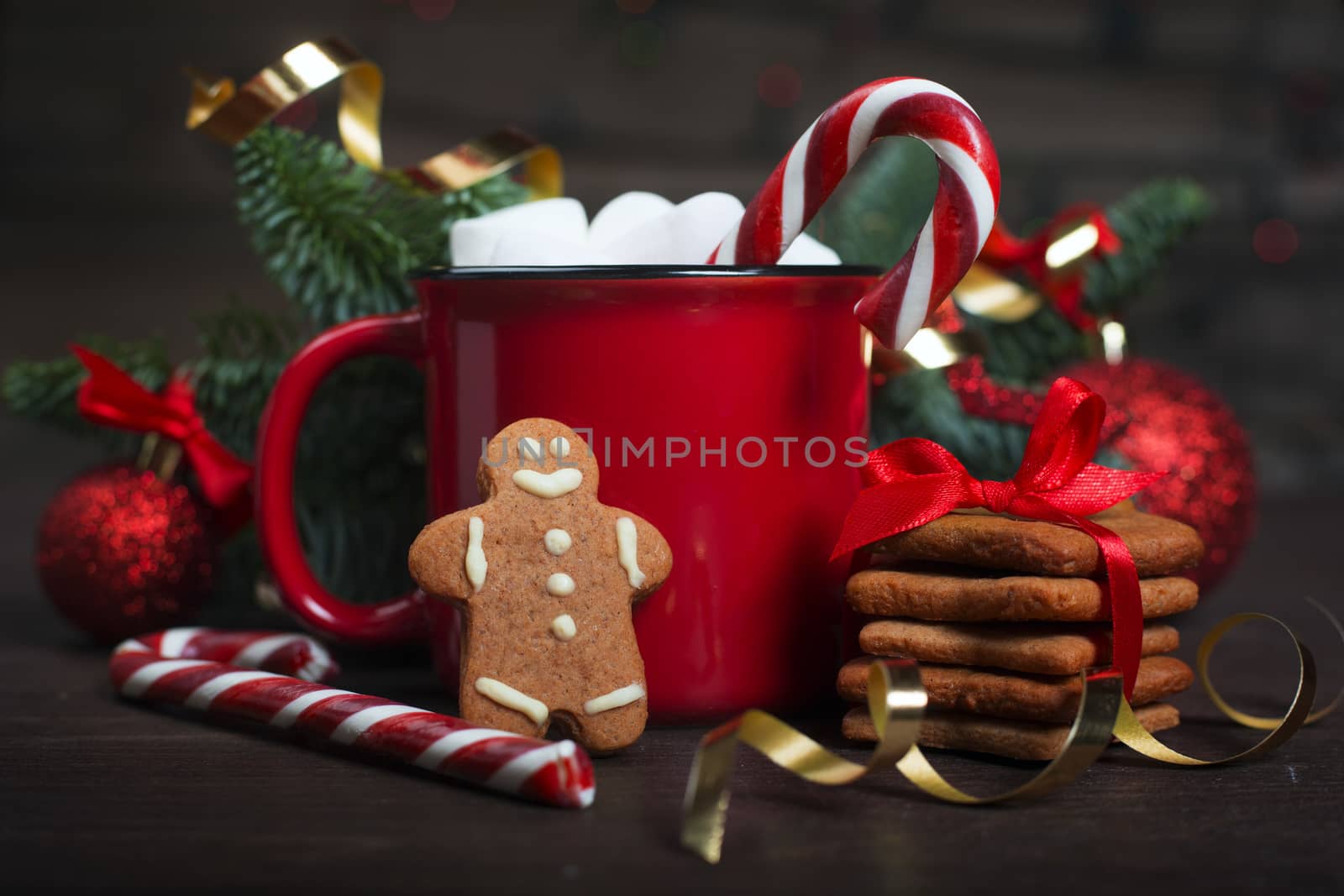 Cocoa in red mug with marshmallows candy cane fir tree branches and red baubles on dark wooden background with bokeh lights