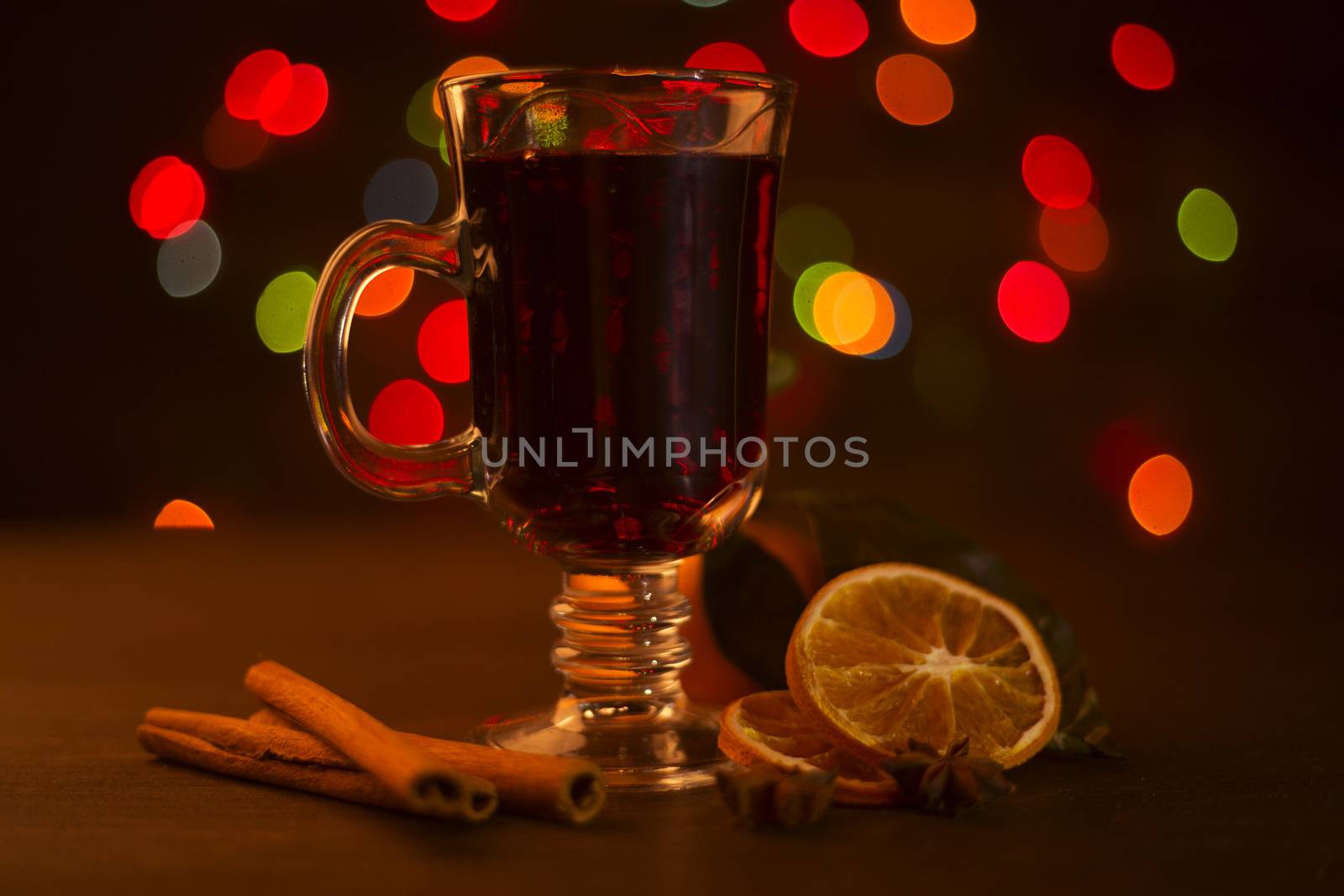 Mulled wine with cinnamon sticks and orange over holiday christmas lights background