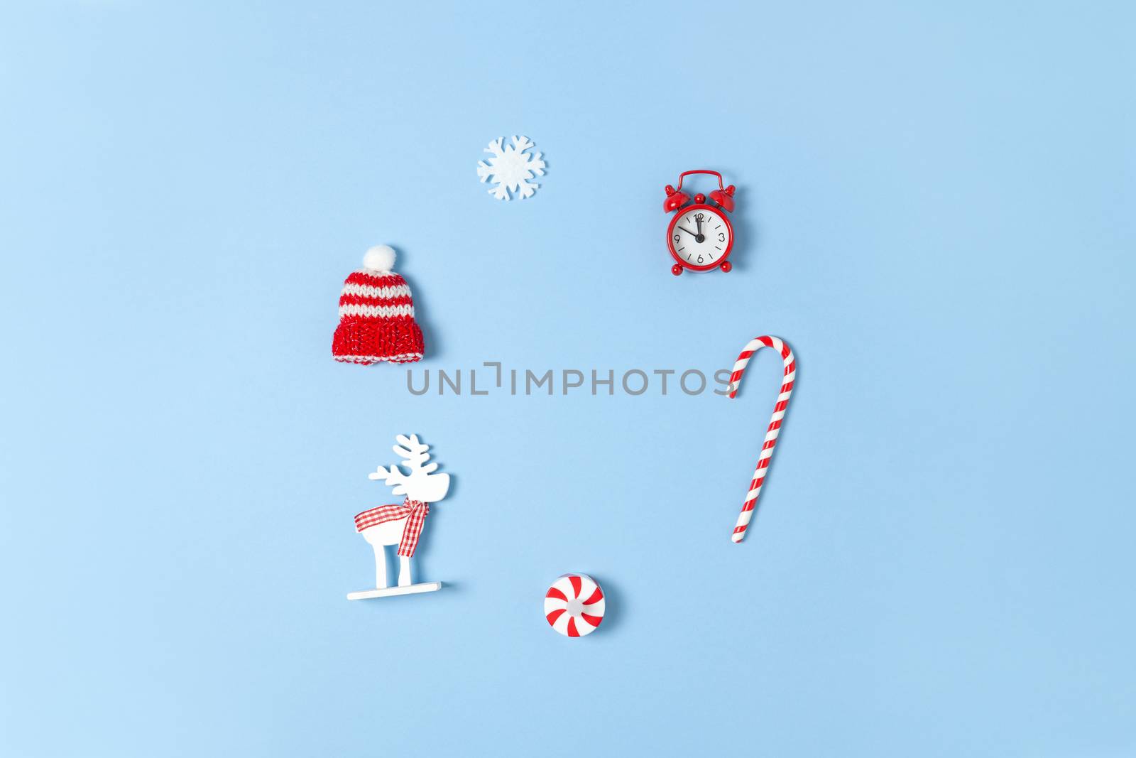 Simple creative Christmas composition. Candy cane, deer, hat, snowflake, red clock on blue background, copy space. Minimal style. Top view. Horizontal. For greeting card, office supplies.