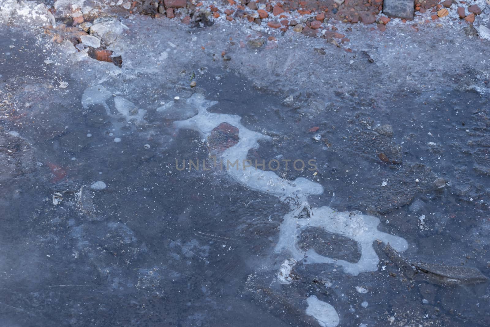 Frozen Puddle with broken ice. Ice Crust On Frozen Puddle. Winter background. Frozen puddle on the road. In January. Frozen Puddle And Dirt Road Close-Up. 