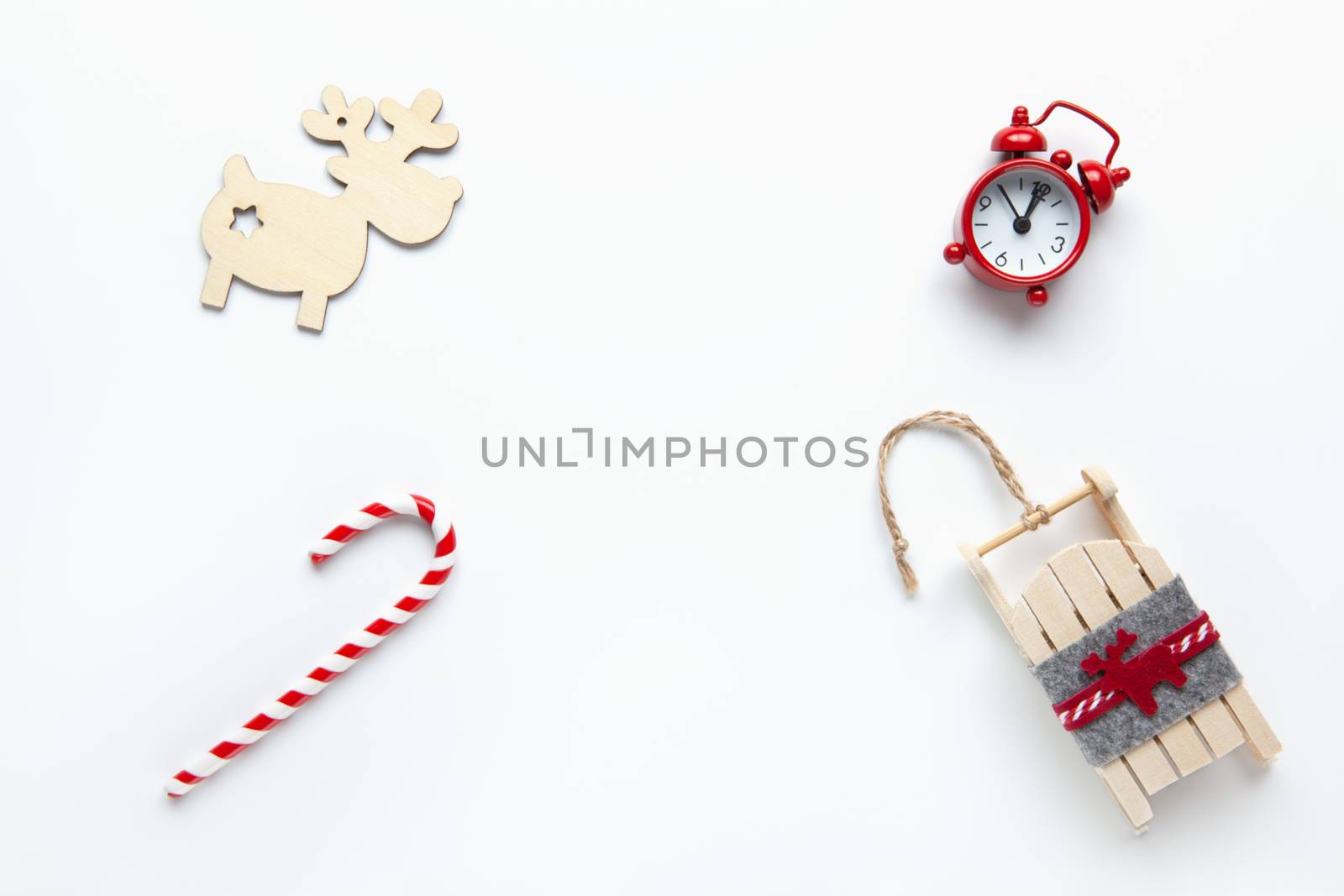 Christmas flat lay, wooden deer, candy cane, small red analog clock, sled on white background, copy space. Minimal style. Top view. Celebration, festive, eco concept. Horizontal.