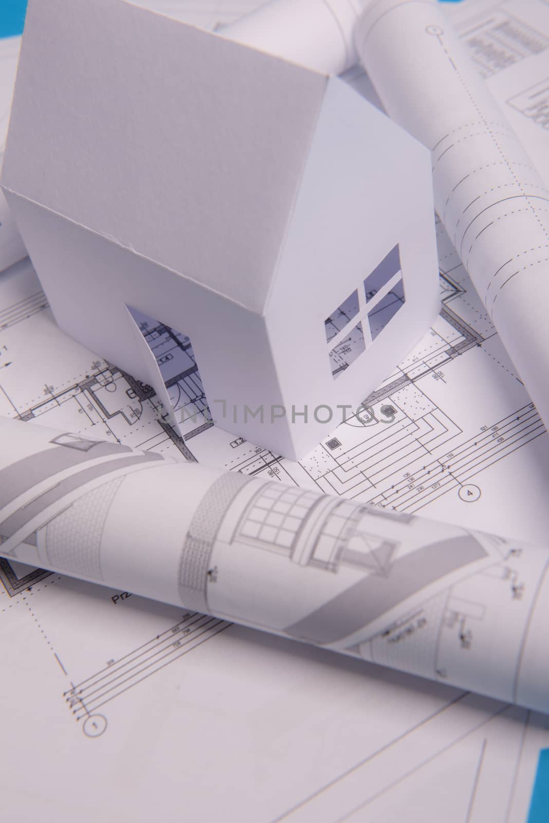 White family paper house, house projects plan and blueprints in the background. Minimalistic and simple concept, style. Horizontal orientation. View from above.