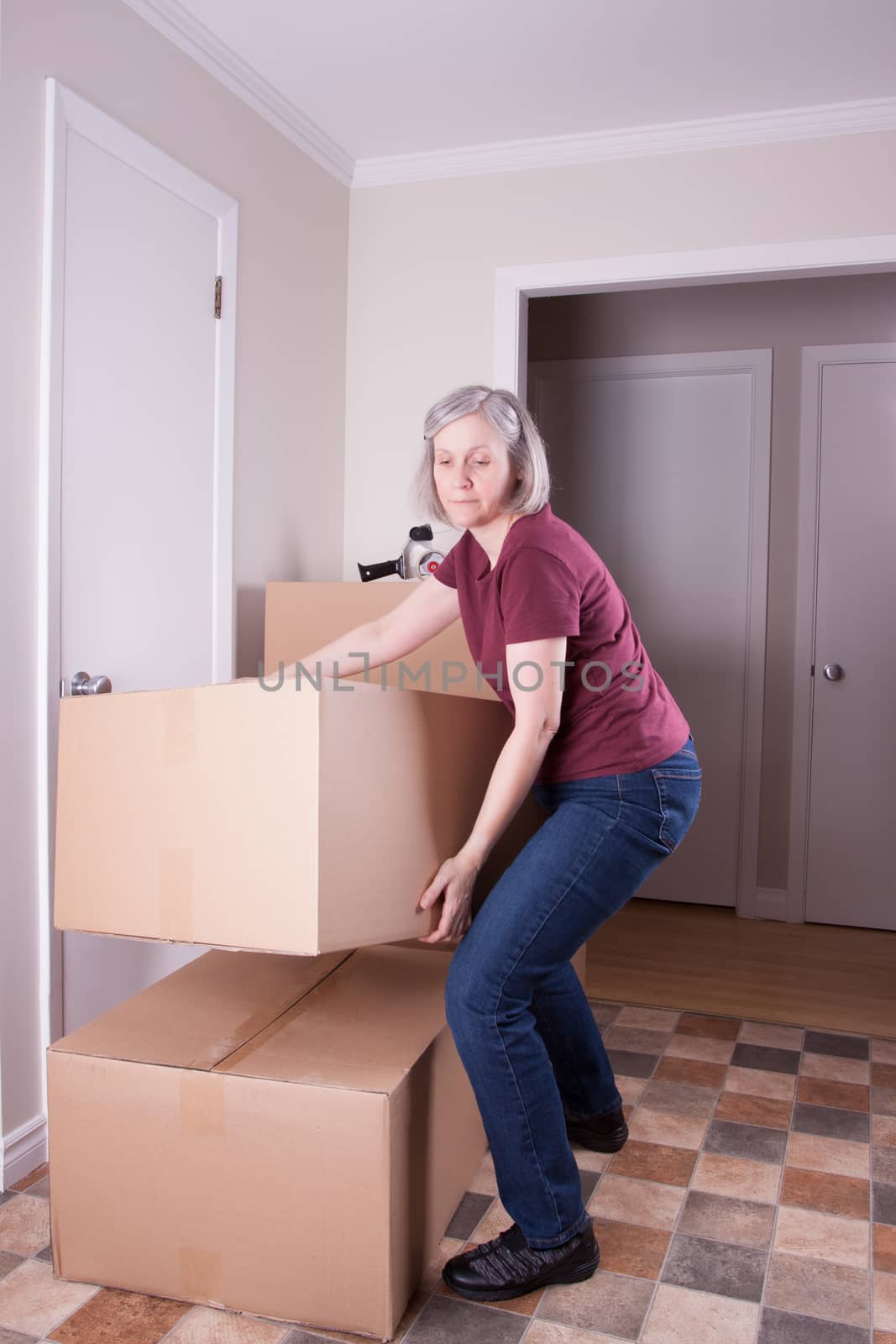 Mature grey haired woman prepares to move to another house stacks big brown boxes