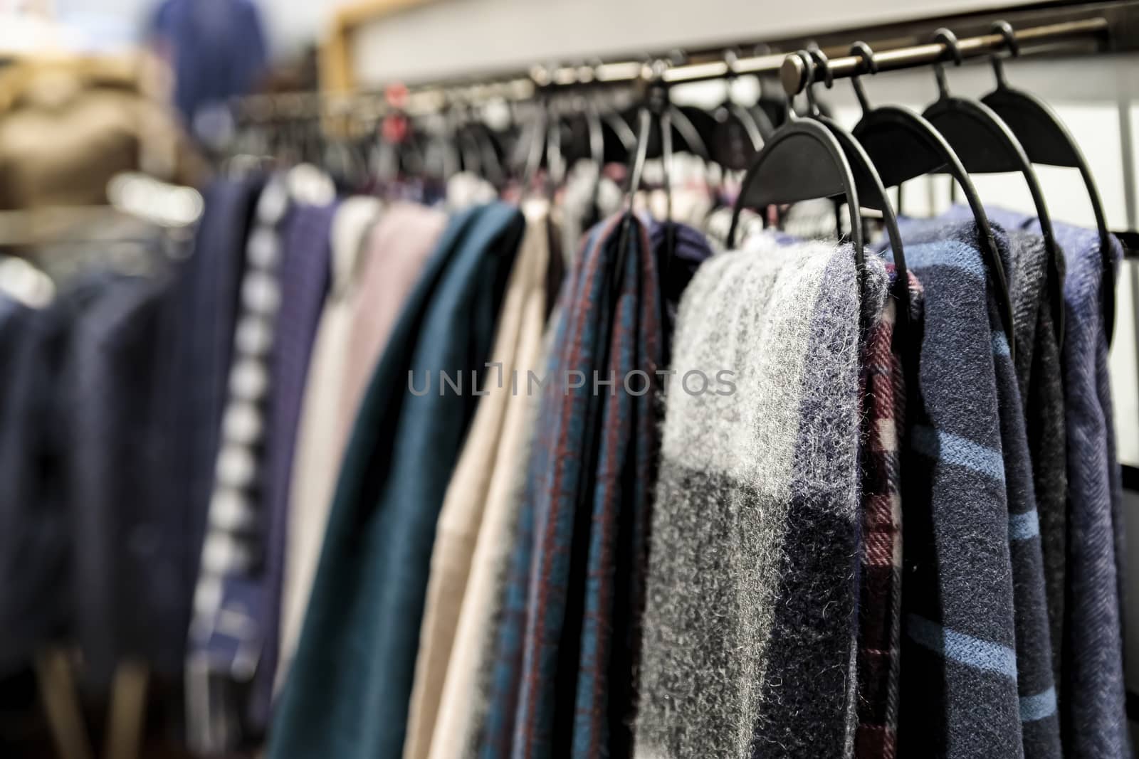 Soft winter scarves in different colors hang on hangers in the store. by bonilook