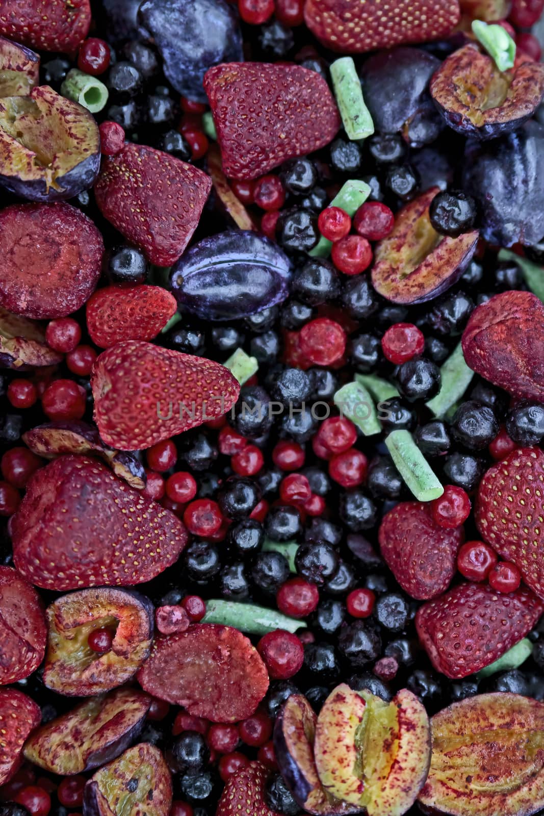 Frozen berries in grocery store shot close-up, blurred background. Multicolored mix of strawberries, plums, currants.