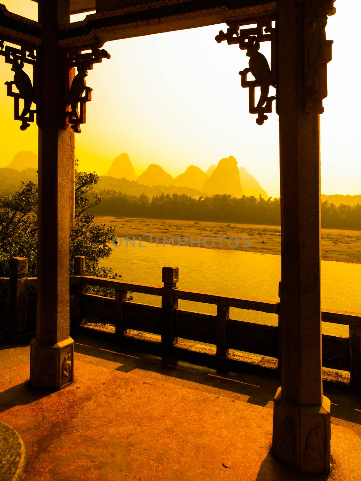 Sunset in karst landscape around Yangshuo an Li River with peaks silhouettes, Guangxi Province, China. View from terrace with ornamental columns.
