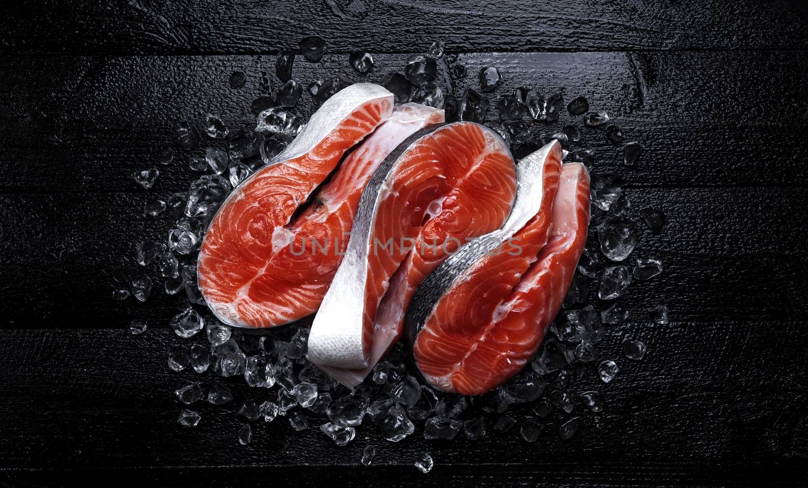 Fresh salmon steaks on black wooden background. Top view by xamtiw