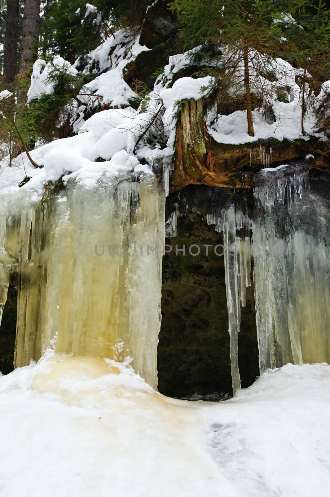 Frozen waterfalls on the rock, orange colored and snow