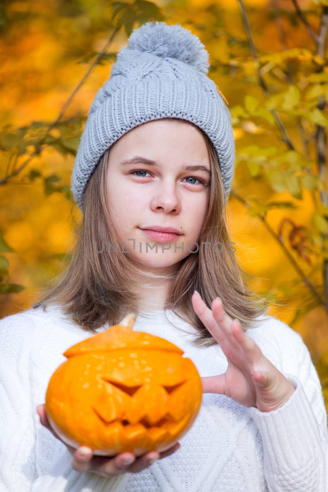 Teenage girl holding halloween pumpkin over orange autumn park background