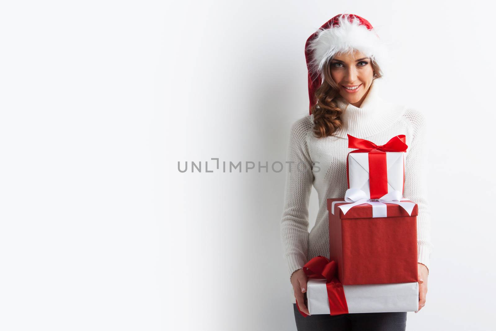 Happy woman in Santa hat with stack of Christmas gifts