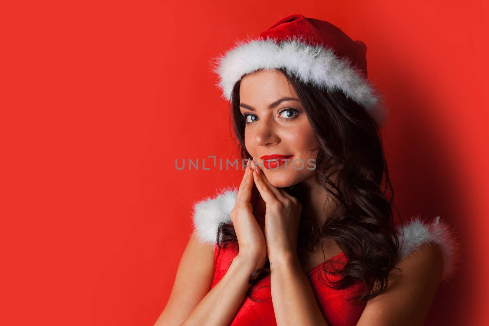 Pretty Pin-up style Santa girl in red hat and dress on red background