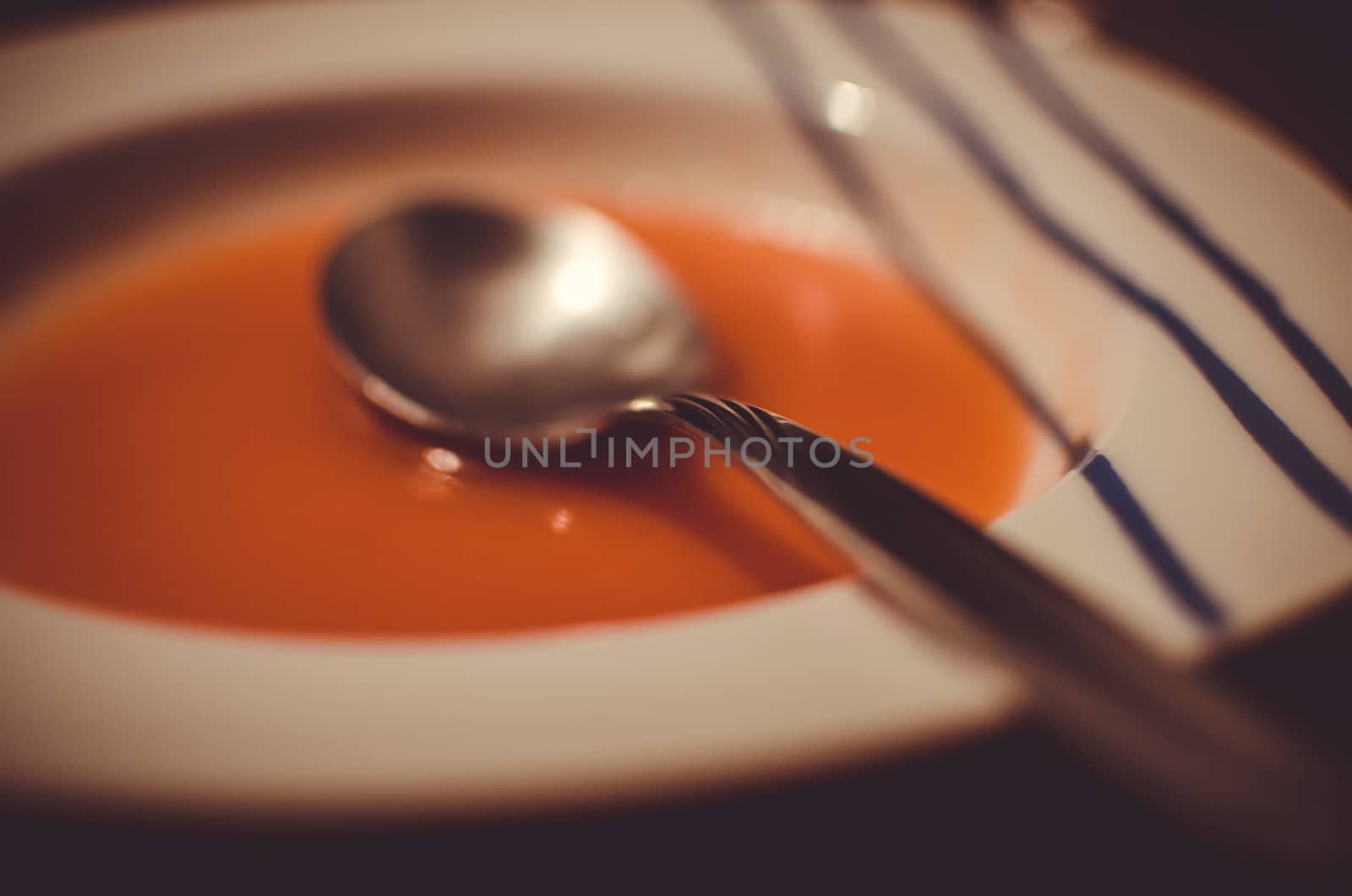 Spoon reveals some waves that are not present in the tomato soup contained in the plate.
