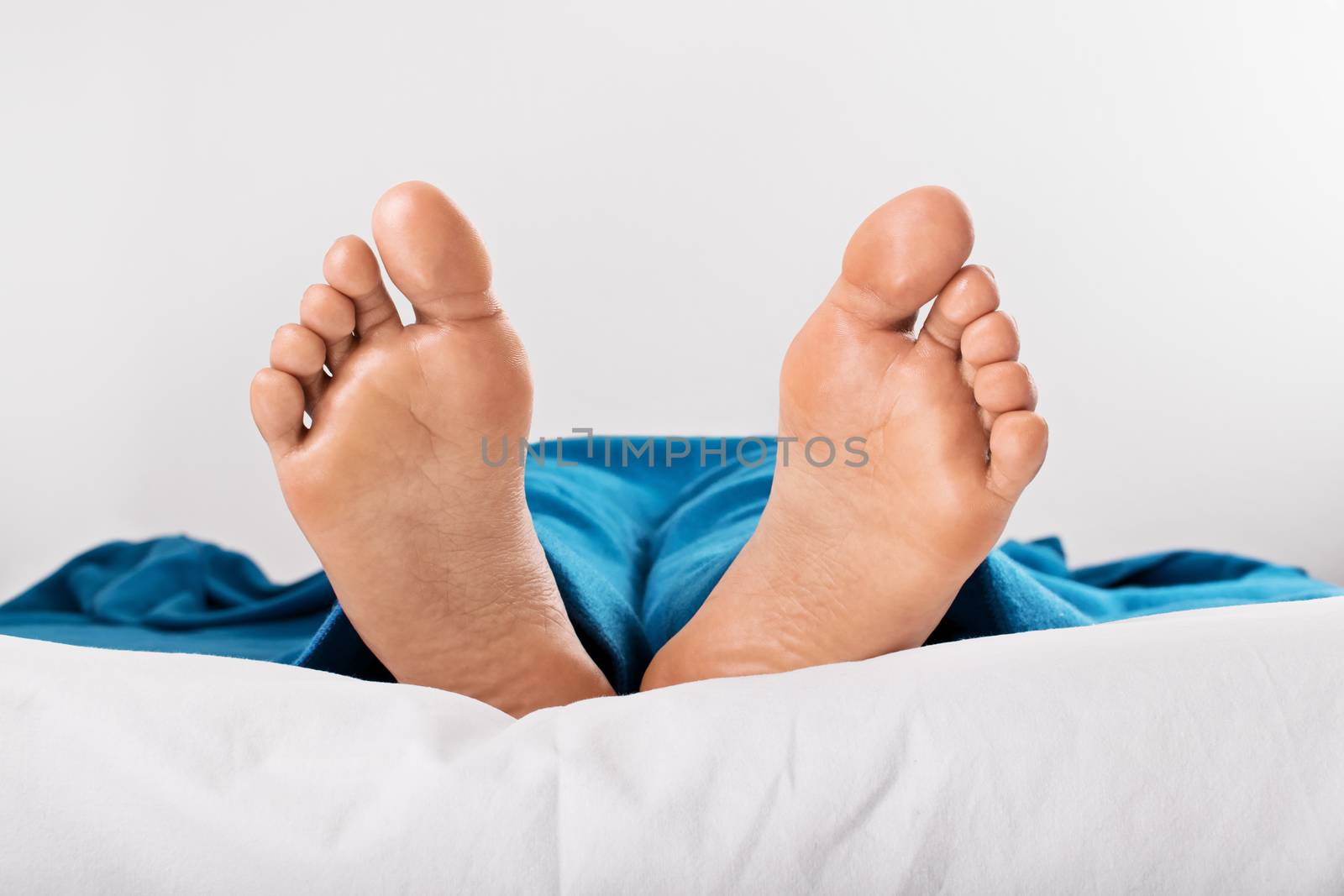 Resting female feet under blue blanket by Mendelex