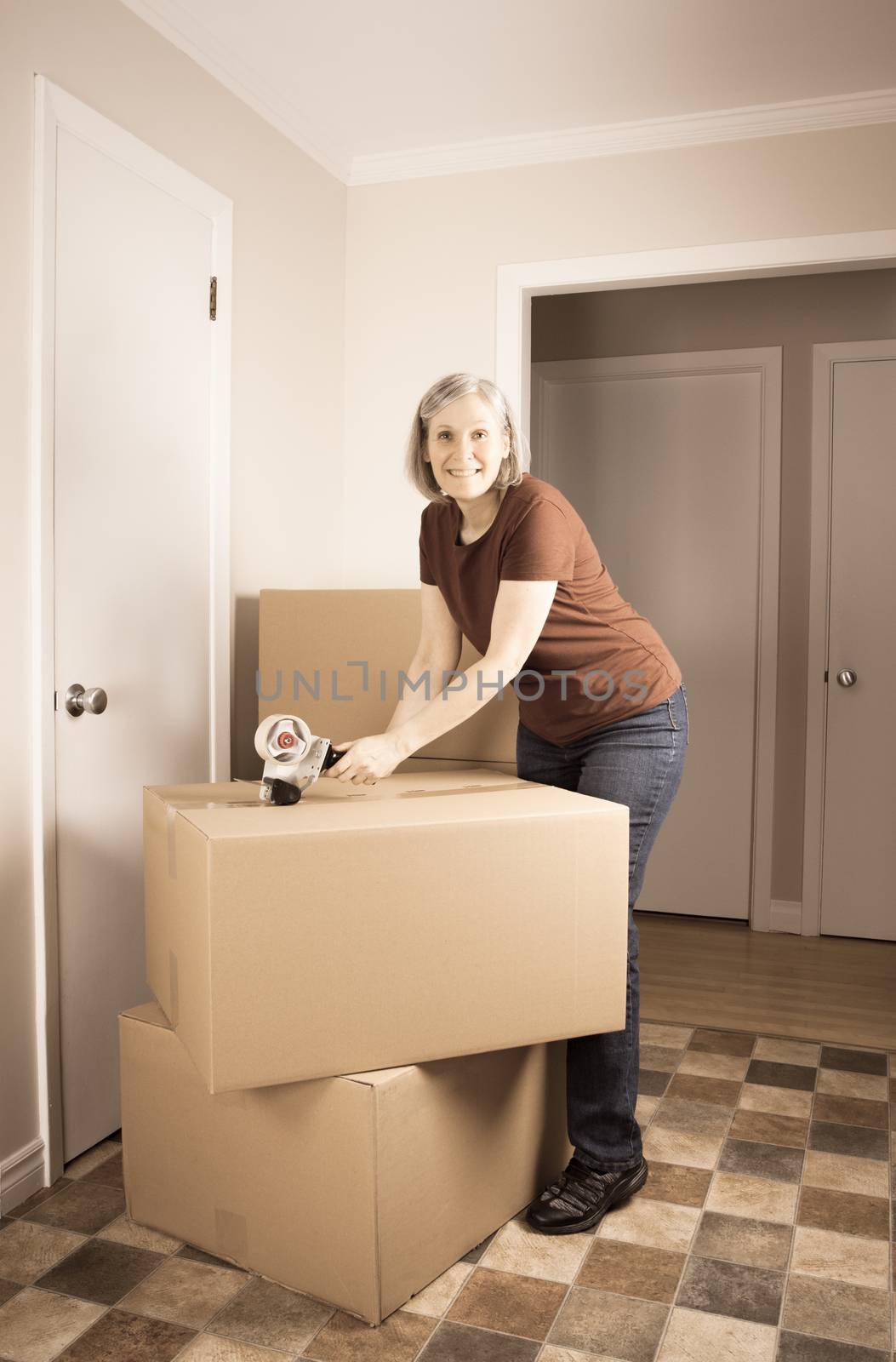 Mature woman closing boxes with tape by lanalanglois