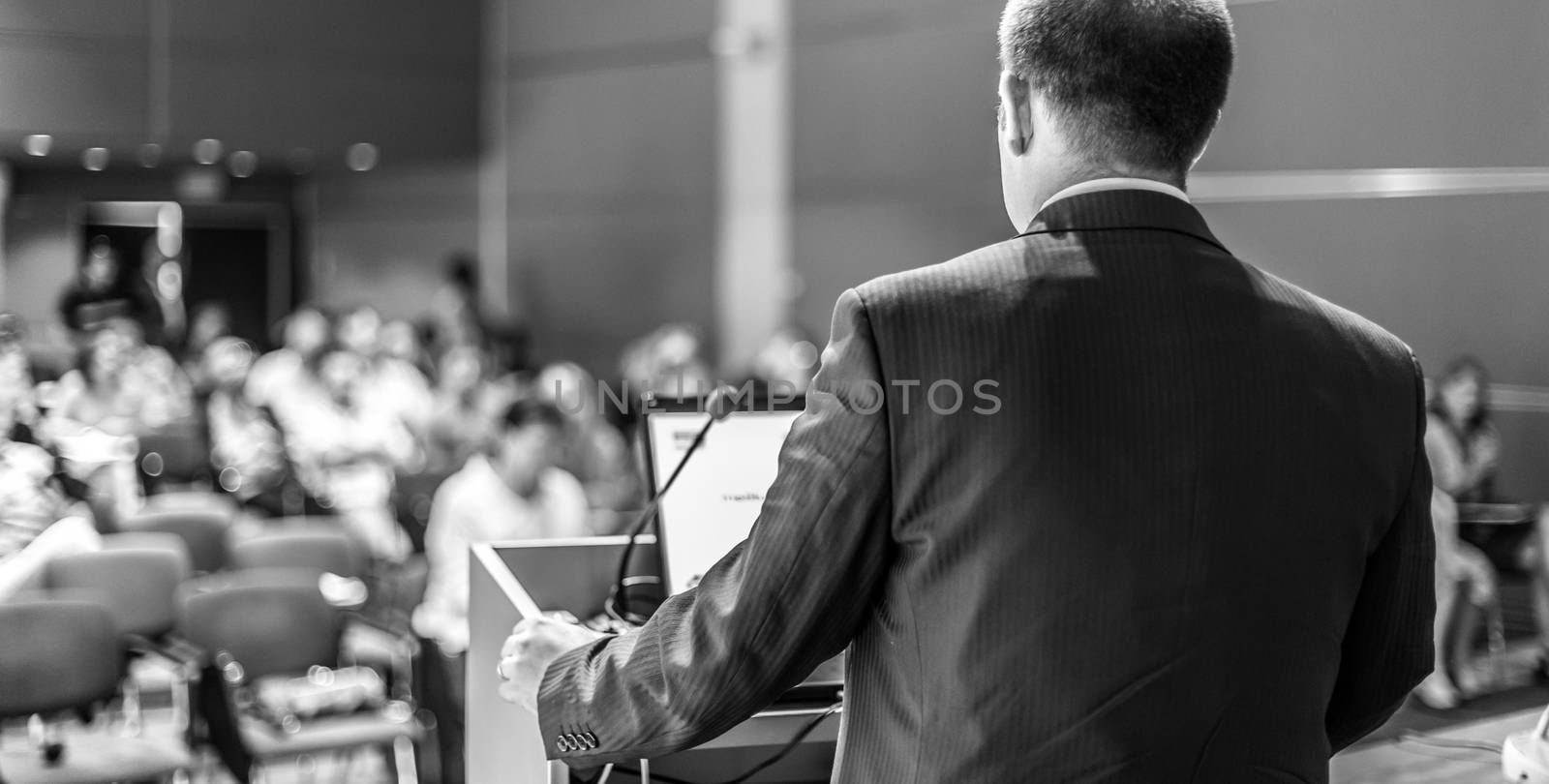 Speaker giving a talk on corporate business conference. Unrecognizable people in audience at conference hall. Business and Entrepreneurship event. Black and white image.