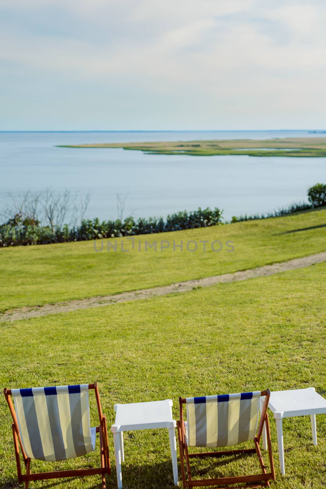 Empty beach chair on meadow on summer time. Sunlight and sea in the background. Coast line