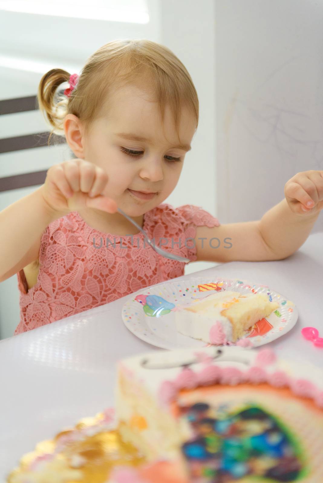 Baby girl 1 year old eating birthday cake in room. Birthday party. Childhood.